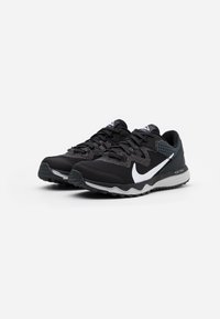 Chaussures de sport noires avec une tige texturée, logo swoosh blanc, semelle grise et motif de grip robuste, conçues pour la course sur sentier.