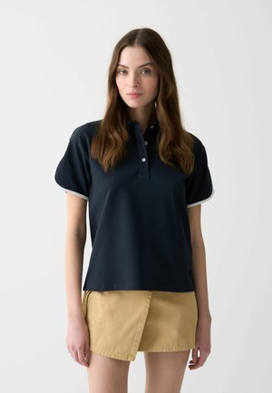 Marine kleurige polo met korte mouwen, voorzien van een kraag en witte details. Zachte, gladde stof met knoopsluiting aan de voorkant.