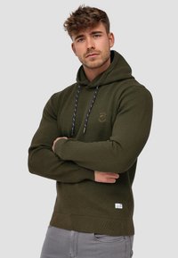 Oliven grøn bomuldshoodie med en front kangaroo-lomme, ribbede manchetter og kant, samt marineblå snore. Har et lille logo på brystet.