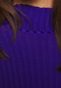 Jasnopurpurowy sweter z dzianiny z wyższym żeberkowym kołnierzem i pionowym teksturowaniem, wykonany z miękkiej, gładkiej tkaniny oraz bezszwowym wykończeniem.