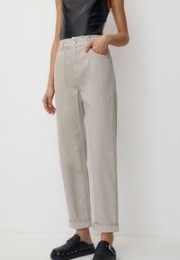 Pantalons gris clair taille haute avec une coupe décontractée, dotés de poches arrière et de revers roulés. Associés à des chaussures noires à enfiler.