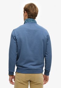 Sudadera azul con cuello y puños acanalados, con un detalle de mezclilla en el escote. Textura suave y diseño de ajuste relajado.