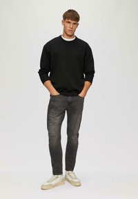 Zwarte sweatshirt met geribbelde cuffs, gecombineerd met vervaagde grijze jeans met beschadigde details en witte sneakers met beige accenten.