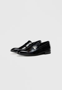 Svarta lackläderloafers med en smidig design, som har ett dekorativt band över fotens medelparti och en låg, rundad klack.