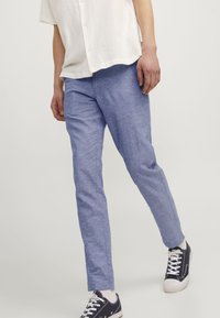 Pantalones de mezcla de lino azul claro con corte recto, que presentan una textura suave y se combinan con zapatillas oscuras.