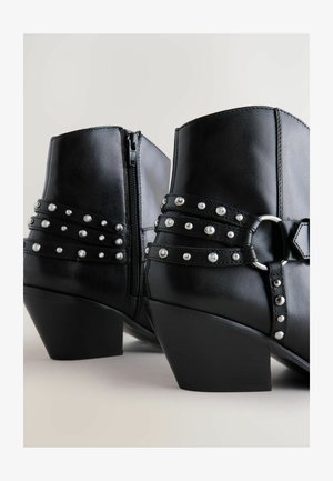 Černé kožené kotníkové boty se zipem, se stříbrnými hroty a dekorativními pásky kolem středu a blokovým podpatkem.