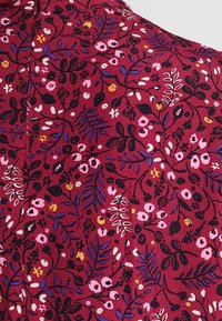 Rødt stof med et blomstermønster med pink, sort og gule accenter, der viser forskellige blade og blomster i et tekstureret design.