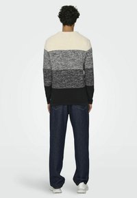 Camicia a maniche lunghe con un gradient orizzontale di crema, grigio e nero, abbinata a jeans blu scuro e scarpe da ginnastica bianche.