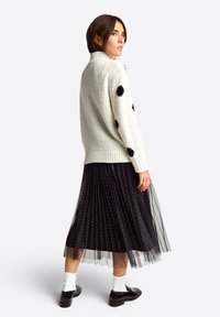 White, textured sweater with black polka dots, paired with a black pleated tulle skirt featuring silver specks. Black shoes and white socks.