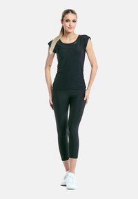 Černé krátké sportovní tričko s kulatým výstřihem, spárované s černými capri legínami. Modelka má na sobě bílé sportovní boty.