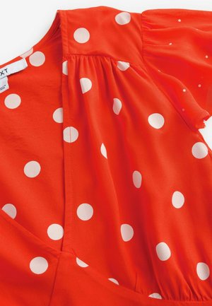 Abito rosso con maniche a sbuffo corte, caratterizzato da grandi pois bianchi. Realizzato in un tessuto leggero con una leggera lucentezza e dettagli arricciati.