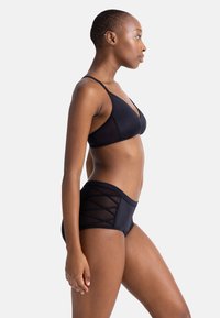 Juodas bikini komplektas, kuriame yra trikampis braletė su plonomis petnešėlėmis ir aukštai aukštu liemeniu kelnaitės su kryžminiu tinklelio dizainu. Lygus paviršius.