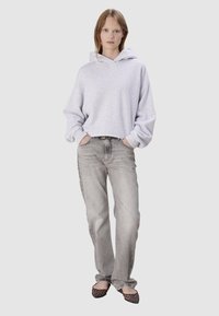 Haut de sweat-shirt oversized gris clair avec une poche avant, associé à un jean droit gris délavé et des ballerines noires à motif léopard. Design et texture simples.
