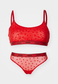 Rød undertøy-sett med en gjennomsiktig bralette og matchende truse. Begge delene har et hjerte-mønster og en svart bærestykke med merke.