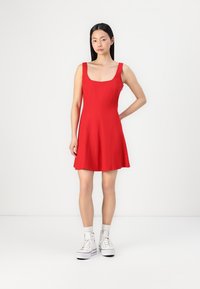 Robe sans manches rouge avec un décolleté carré, jupe évasée, fabriquée en tissu léger, associée à des baskets plateforme blanches et des chaussettes.