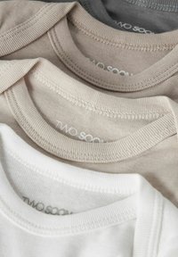 Pile de chemises à col ras du cou côtelées pliées en blanc, beige et gris, montrant la texture du tissu et les détails des coutures.