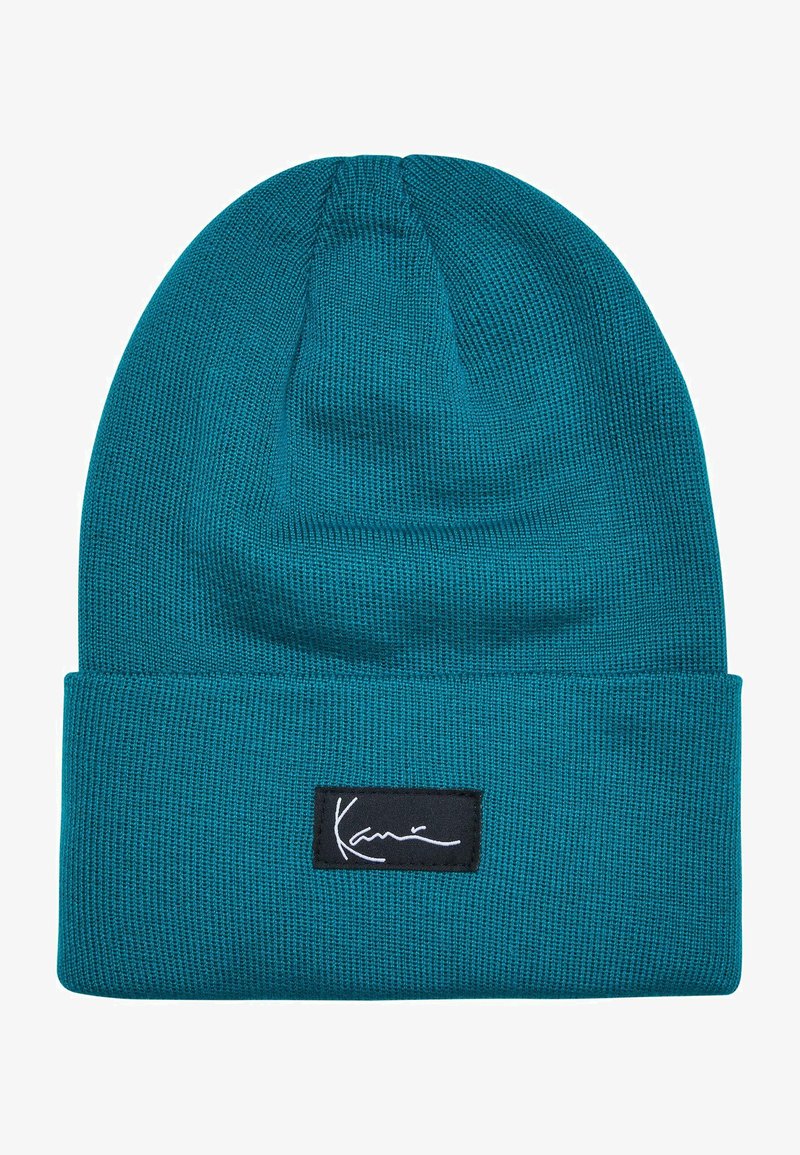 Tyrkysová pletená čepice s ohnutým lemem. Obsahuje černou obdélníkovou nášivku s bílým podpisovým stehem. Měkká textura, pružný materiál.