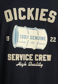 T-shirt en coton bleu marine foncé avec un graphique rétro d'un design de tuyau, comportant le texte "DICKIES", "SERVICE CREW" et "100% GENUINE" en crème et bleu clair.
