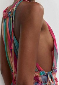 Robe sans manches rayée colorée avec un dos bas, présentant des bords froncés et des liens. Les couleurs prédominantes incluent le rose, le bleu et le vert.