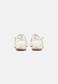 Silver metallic sandals with a flat sole, featuring cross straps and an adjustable buckle. Smooth texture and minimalistic design.