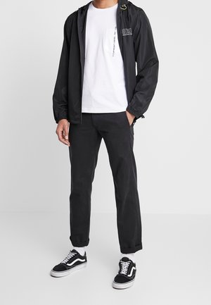 Mustava kevyt takki, jossa on kiristettävä huppu, valkoinen t-paita, mustat housut ja mustat lenkkarit valkoisilla yksityiskohdilla. Yksinkertainen muotoilu ja rento istuvuus.