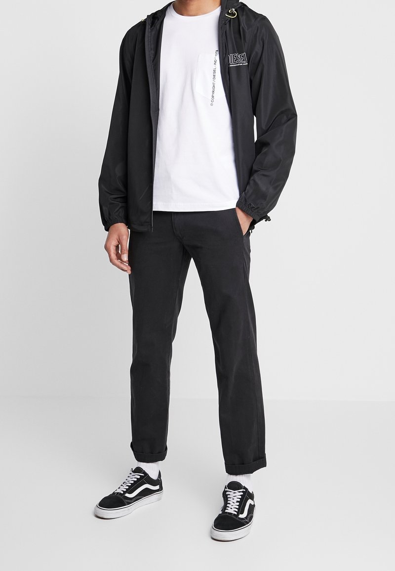 Svart lättviktig jacka med dragsko i huvan, vit t-shirt, svarta byxor och svarta sneakers med vita accenter. Enkelt design och avslappnad passform.