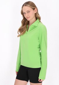 Langærmet, halvlynlås pullover i lys grøn, lavet af blødt materiale; har en krave og en glat tekstur, der matches med sorte shorts.