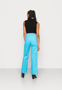 Top sem mangas de malha preta combinado com calças altas de cor azul clara. A modelo usa botas de salto pretas, vista de costas.