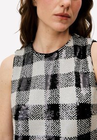 Zwart-wit mouwloos top met een geruit patroon van pailletten, met een gladde textuur, een ronde halslijn en een subtiele glans.