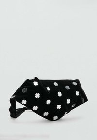 Marsupio in velluto nero con borchie circolari riflettenti color argento sparse e chiusura con cerniera su uno sfondo semplice.