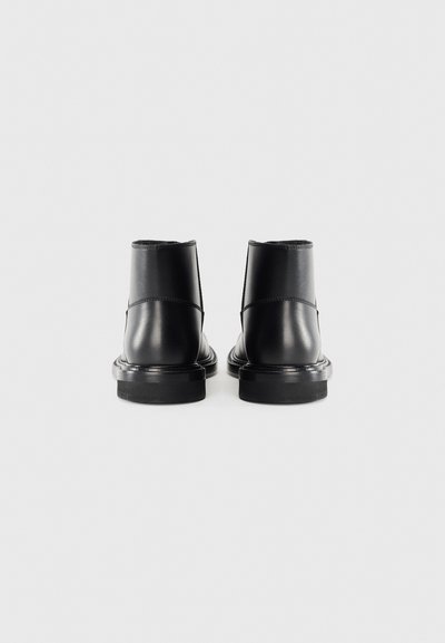 Botas de cuero negro hasta el tobillo con un acabado liso, punta redonda, tacón bajo apilado y un detalle de costura minimalista en los laterales.