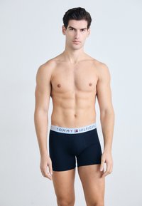 Boxeri din bumbac negri cu un elastic alb ce poartă logo-ul "TOMMY HILFIGER" și accente în roșu, alb și albastru. Textură netedă.