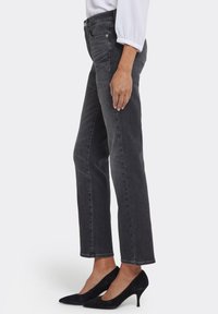 Grå denimjeans med rak benpassform, midjeficka och subtila blekningsdetaljer, kombinerade med svarta spetsiga klackskor. Texturen är mjuk.