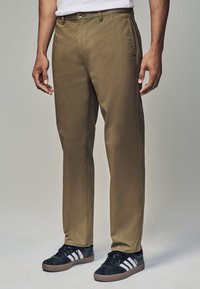 Kaki byxor tillverkade av slitstark tyg, med rak passform, sidofickor och knappstängning. Matchas med svarta sneakers.