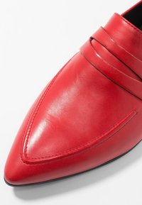 Scarpa rossa in pelle con design a punta, dotata di due cinturini orizzontali sulla tomaia e una texture liscia e lucida.