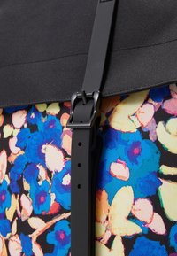 Tissu à motif floral dans des teintes vives de bleu et de rose, avec un rabat en tissu noir et un détail de sangle à boucle noire. Surface texturée.