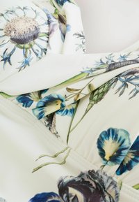 Blumendruckstoff mit blauen und grünen Blumen auf einem cremefarbenen Hintergrund, mit einer weichen, schlaffen Textur und sichtbaren Nähdetails.