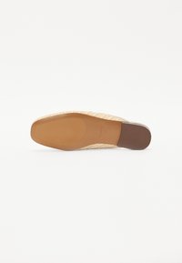 Suola in espadrille con una tomaia intrecciata beige, caratterizzata da una soletta piatta e testurizzata e una base in gomma marrone chiaro per maggiore stabilità.
