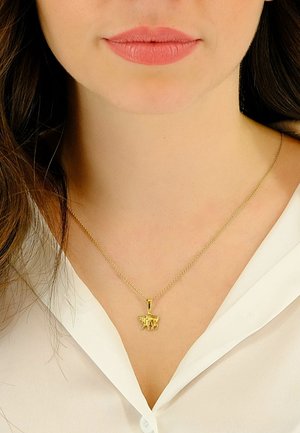 Collier pendentif en or avec un motif de vache sur une chaîne délicate, porté sur une chemise blanche, mettant en valeur les détails complexes et l'éclat.