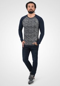 Langermet t-skjorte med en teksturert grå kropp og marineblå raglanermer. Kombinert med mørke jeans og grå sportsko.