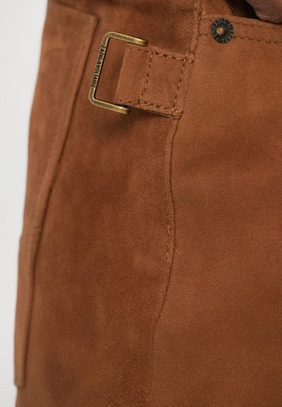Matériau en daim marron au toucher lisse, avec une boucle en métal doré et des détails de couture visibles à la taille.