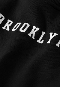 Primer plano de tela negra con letras capitales blancas que forman la palabra "BROOKLYN" en una disposición curva.