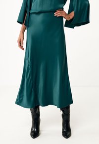 Turkusowa satynowa sukienka o zwiewnym kroju, z bufiastymi rękawami i detalem po bokach. W zestawie z czarnymi kozakami do kolan.