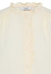 Blouse crème avec col montant à volants et devant boutonné avec des boutons recouverts de tissu et une délicate bordure verticale à volants.