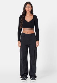Musta ribattua lyhythihainen crop-top, jossa on V-pääntie, yhdistettynä väljiin mustiin cargo-housuihin, joissa on sivutaskut.