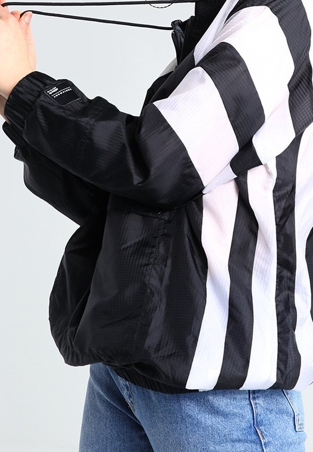 Svart- och vitrandig vindjacka med dragkedja fram, snörning i huvan och elastiska ärmmuddar. Tillverkad av lätt, glänsande tyg.