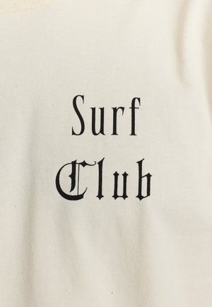 T-shirt in cotone di colore crema con una scritta nera che recita "Surf Club" in un font dallo stile vintage.