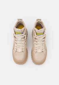Paire de baskets montantes Buffalo beiges avec semelles épaisses, languettes blanches à motif, et semelles intérieures jaunes sur fond blanc.