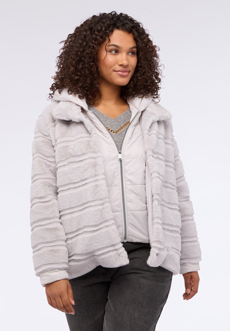 Jasnoszara kurtka z sztucznego futra w poziome paski, z kapturem i otwartym przodem. Noszona na szarym pikowanym kamizelce.