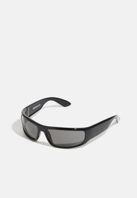 Lunettes noires avec une finition brillante, design enveloppant et verres gris. Présence de la marque sur les branches et une monture robuste.